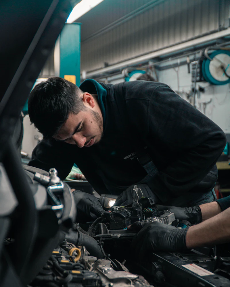 A technician leaning over an open engine bay, working on the engine