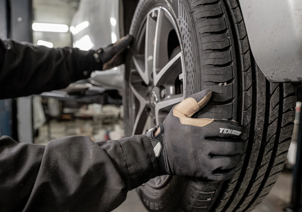 A technician in work gloves fitting a tire onto a car on a lift